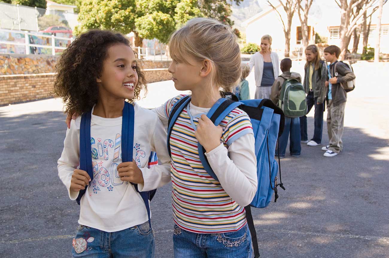 An image of two children sharing a happy moment with children and a teacher in the background.